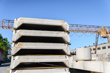 A stack of reinforced concrete slabs against a blue sky and a yellow crane.