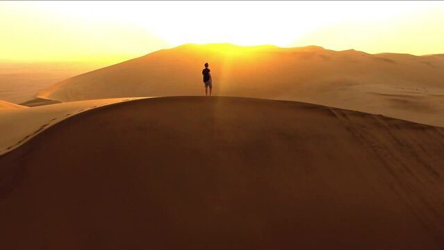 Sunset, drone and man walking in desert for hiking, adventure and freedom. Travel, discover and expedition hobby with person silhouette thinking on sand dunes hill for explorer, vacation and journey