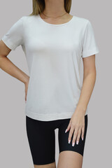 Cropped image of a young girl in a blank white t-shirt and black shorts, on a light background. Layout, mocap, free space for text, logo.