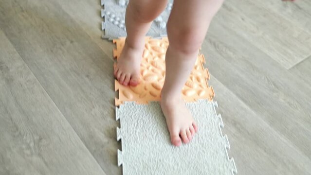 The child walks on an orthopedic massage mat for legs of different hardness and texture. Massage of the nerve endings of the legs, prevention of flat feet in children. Foot deformity treatment.