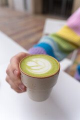Man Hands Holding Macha Latte Cup with Wooden Plate in Caffe