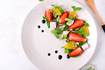 Salad with strawberry, orange, red wine soaked cheese, Romaine lettuce leaves and pine nuts on white plate with copy space. Top view