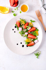 Salad with strawberry, orange, red wine soaked cheese, Romaine lettuce leaves and pine nuts on white plate with copy space. Top view