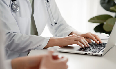 Doctor and patient sitting at the desk in clinic office. The focus is on female physician's hands...