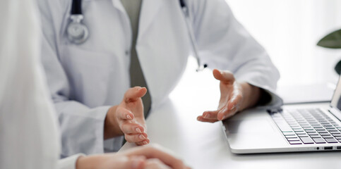 Doctor and patient sitting at the desk in clinic office. The focus is on female physician's hands...