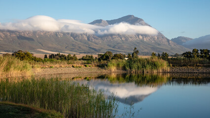 View of a mountain with low white clouds and a dam with the mountain reflection in the dam