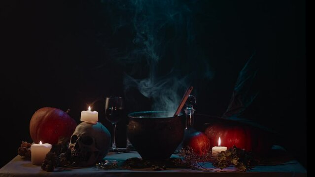 Halloween theme still life. Pumpkins, smoking cauldron, skull, candles in dark