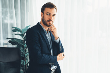 Handsome businessman in black suit stand confidently in his modern office portrait, deep in thought...