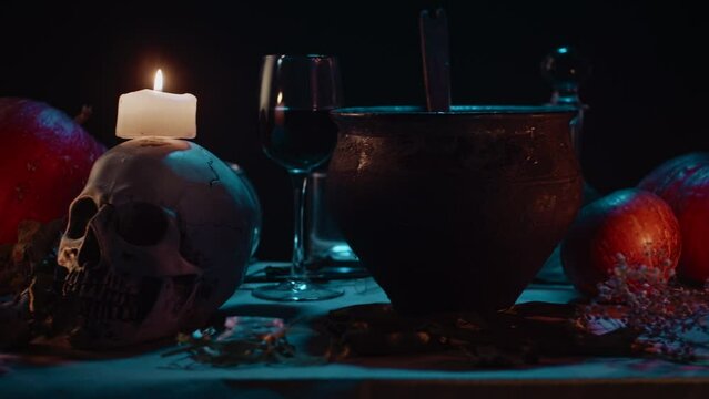 Halloween theme still life. Pumpkins, smoking cauldron, skull, candles in dark. Slider motion