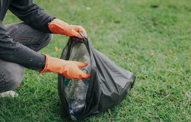 Male hand picking up plastic waste to clean up at the park.