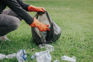 Male hand picking up plastic waste to clean up at the park.