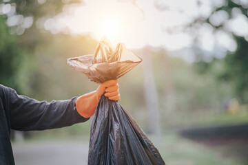 Male hand picking up plastic waste to clean up at the park.