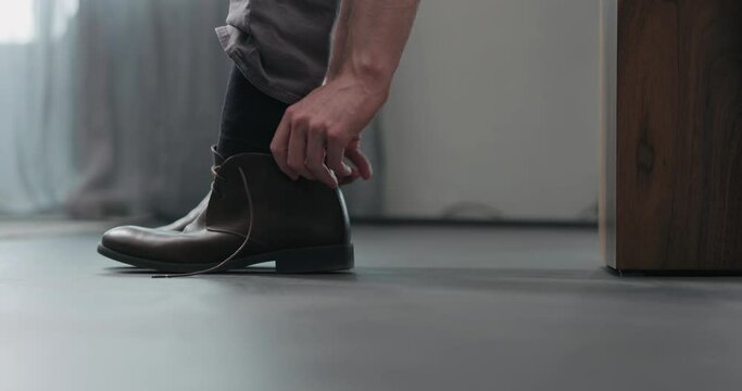 Slow motion young man put on his brown leather chukka boots indoor