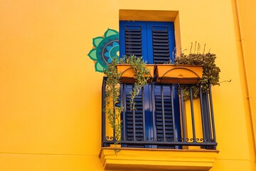 House with a bright yellow exterior, blue windows and balcony adorned with flowers to bring life to...