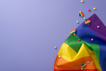 Get ready for Pride Month with this top view flat lay of parade symbolic accessories on a violet background, including rainbow flags, pin badges, and hearts, with space for text or advert