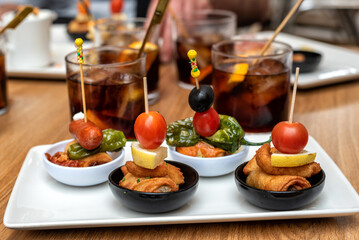 Tapa de pinchos típicos de la gastronomía española, acompañados de unos vasos con vermut de fondo