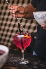 The professional bartender pouring and preparing red gin and tonic drink with strawberry and lime at the bar counter