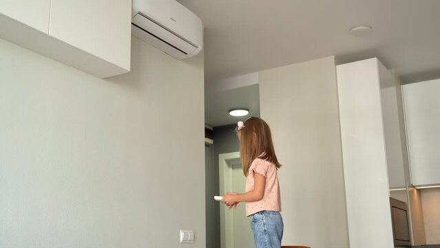 Little girl turn on air conditioner using remote control. Adjust comfortable temperature of cooler system