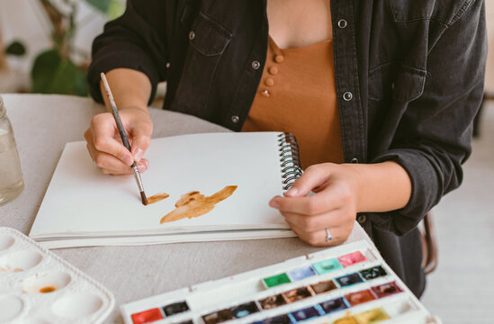 Close-up of an artist sitting at a table painting with watercolor paints