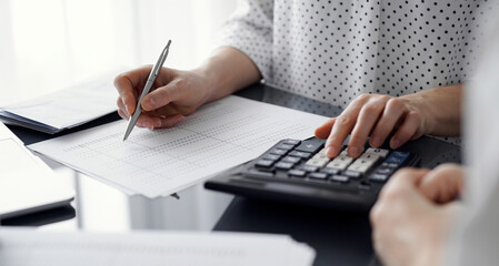 Woman accountant using a calculator and laptop computer while counting taxes for a client. Business audit concepts