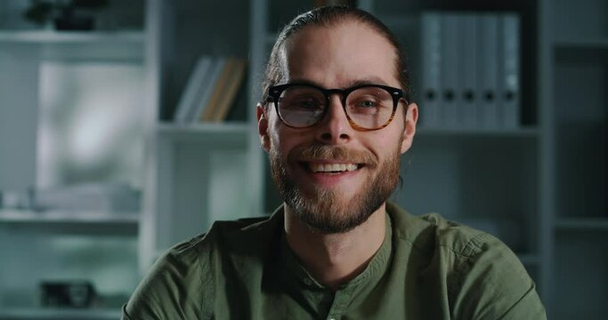 Portrait of a pleasant young guy putting glasses on and looking at camera.