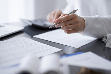 Woman accountant using a calculator and laptop computer while counting taxes for a client. Business...