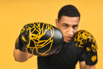 Angry Fighter. Aggressive young african american sports man in boxing gloves isolated over yellow...