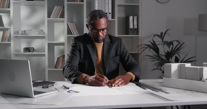 Portrait of a watchful architect drawing blueprints in his office.