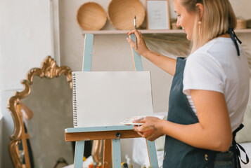 Woman standing at an easel with blank canvas painting with watercolour paints.