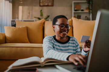 African american woman using credit card and a laptop while online shopping at home