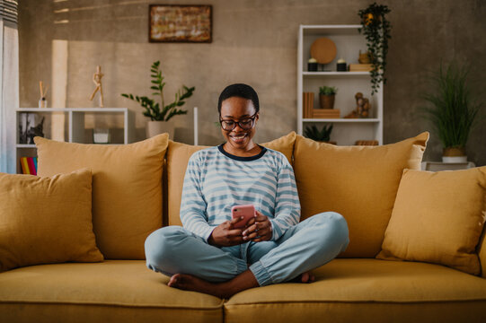 African american woman using a smartphone while sitting on a yellow sofa at home