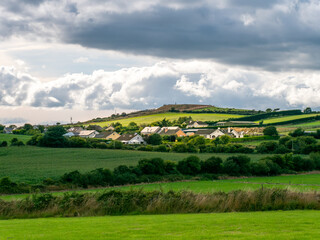 Sky with cumulus clouds over a Irish village on a summer evening. Irish settlement in County Cork, dramatic landscape. European countryside, rustic landscape. Green grass field under cloudy sky