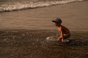 Child have fun on the seashore, splashes in all directions. Happy Summer Holiday. A fun vacation. Family Sea Vacation.