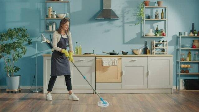 Creative Woman is Washing Floor With Mop and Dancing in Kitchen at Home.Happy Young Woman Cute Housewife is Listening to Music and Dancing During Domestic Work. Household Chores Concept.