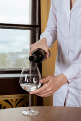 Waitress in a white uniform pours water in a glass in a restourant.