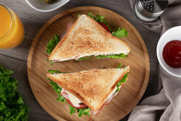 A delicious sliced sandwich with ham, fresh lettuce and tomatoes is served on a plate. View from above.