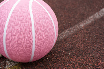 Pink basketball ball on the ground. Close-up ball on the red court. Basketball on the street or indoor court. Sports gear without people. Minimalism. Template, sport background