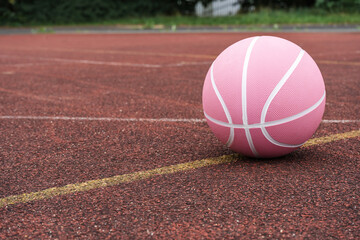 Pink basketball ball on the ground. Close-up ball on the red court. Basketball on the street or indoor court. Sports gear without people. Minimalism. Template, sport background