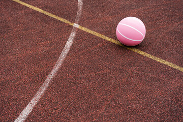 Pink basketball ball on the ground. Close-up ball on the red court. Basketball on the street or indoor court. Sports gear without people. Minimalism. Template, sport background