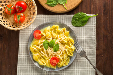 Pasta in a creamy sauce with cheese with a fork next to tomatoes, a knife and greens on a linen napkin.