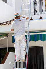 Pintor subido en una escalera pintando la fachada de una casa.
