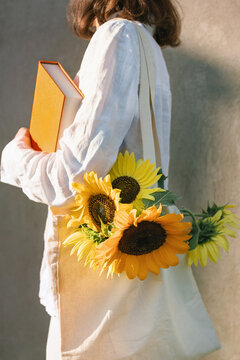 Side view of a girl with sunflowers in a cotton bag and a hardcover book in her hand