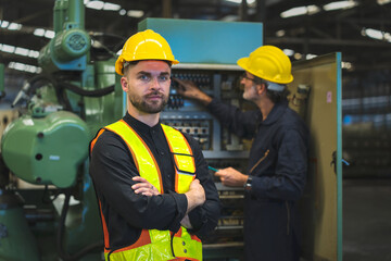 operating staff Standing smiling like an executive, in the background is an employee inspecting an electrical system control machine of an industrial factory., Middle-aged male employee, white skin.
