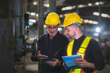 Two operators inspecting machines in industrial factory, holding documents and tablet for check, background in industrial warehouse., middle-aged male worker, Caucasian.