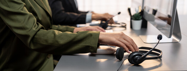Panorama focus hand holding headset on call center workspace desk with blur background of operator team or telesales representative engaging in providing client with customer support service. Prodigy