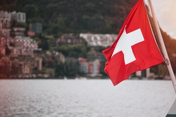 Switzerland flag is waving on a toursitic boat on Lugano lake. A red flag with a white cross on it
