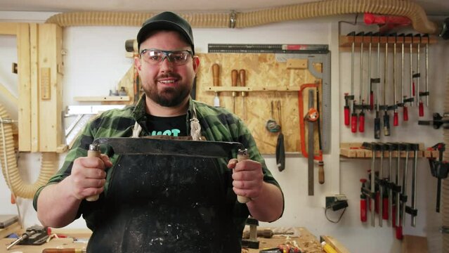 Portrait of a carpenter holding a draw-shave wood carving tool in a woodworking studio. High quality 4k footage