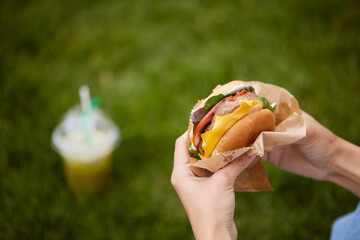 a young girl takes out a burger from a paper bag sitting on the green grass, the concept of food...