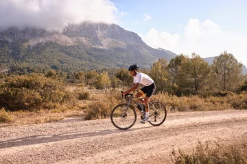 Foto op Canvas Cyclist practicing on gravel road.Fit male cyclist riding a gravel bike on a gravel road with a view of the mountains, Alicante region of Spain © Ketrin