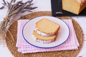 Two slices of lavender and lemon sponge cake on white plate. Small bouquet of lavender flowers on the white table.